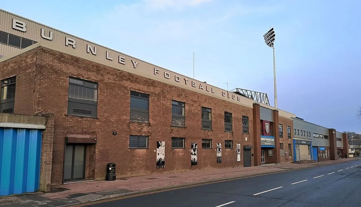 Cận cảnh mặt ngoài sân vận động Turf Moor từ Harry Potts Way, thể hiện kiến trúc cổ kính và uy nghi của sân nhà Burnley FC, một di sản của bóng đá Anh.