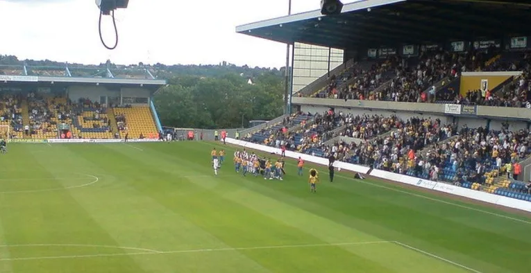 Không khí cuồng nhiệt trên khán đài sân vận động Field Mill trong ngày diễn ra trận đấu của Mansfield Town, cổ động viên tràn ngập sắc vàng và xanh.