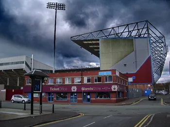 Khung cảnh sân vận động Turf Moor nhìn từ khán đài với thảm cỏ xanh mướt, mái che và các khu vực ghế ngồi đặc trưng của sân nhà Burnley FC tại Ngoại hạng Anh.